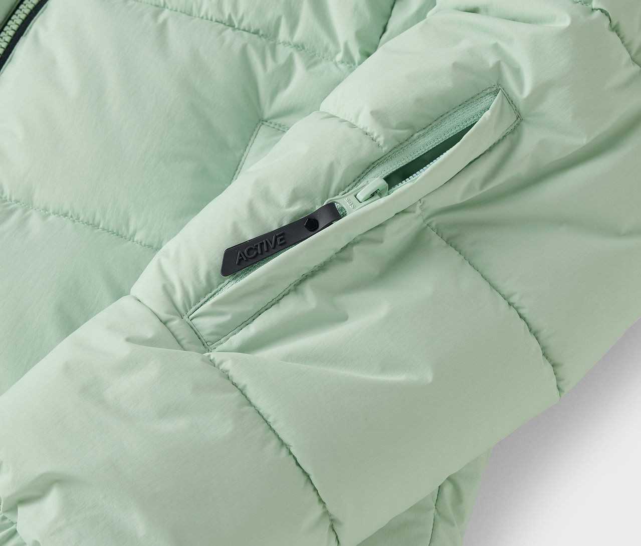 Zbliżenie jasnozielonej kurtki puchowej z kieszenią na zamek.