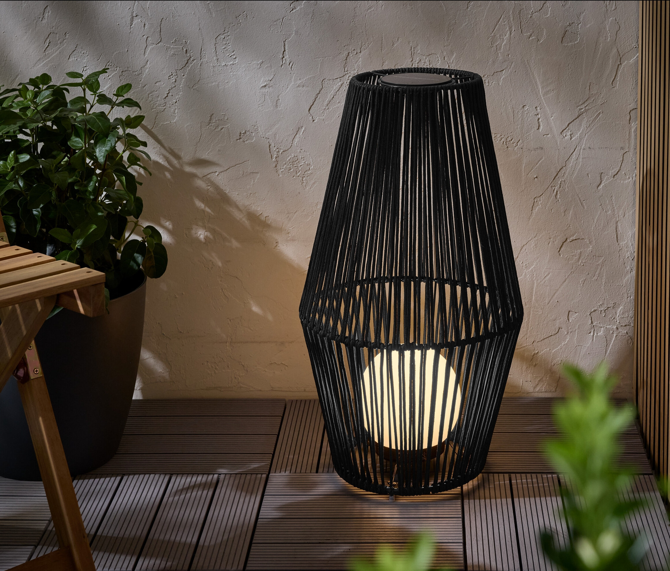 Duża latarnia solarna ze sznurkiem tekstylnym stoi na tarasie.