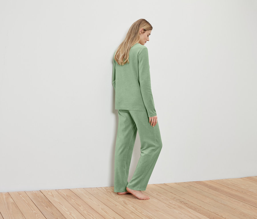 Blondynka w jasnozielonej piżamie stoi tyłem do ściany.