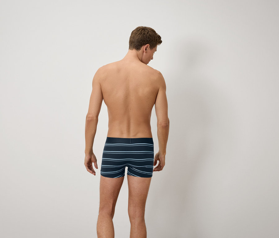 Mężczyzna tyłem do kamery ma na sobie niebieskie bokserki w paski.