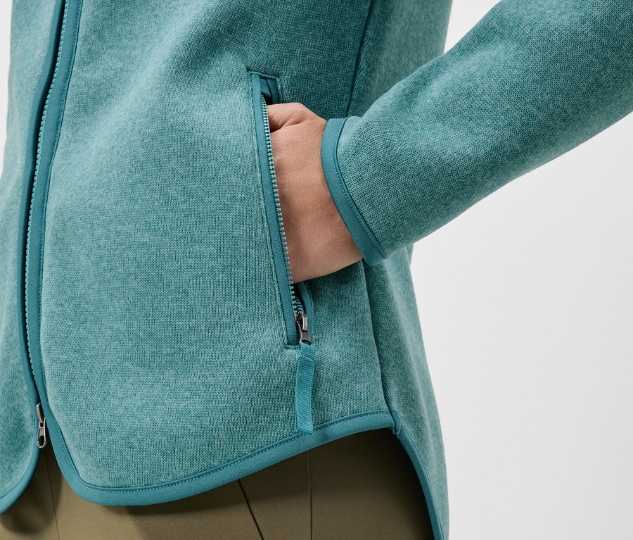 Zbliżenie na turkusową bluzę polarową z ręką w kieszeni.