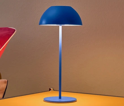 Niebieska akumulatorowa lampa stołowa LED na żółtym stoliku nocnym.