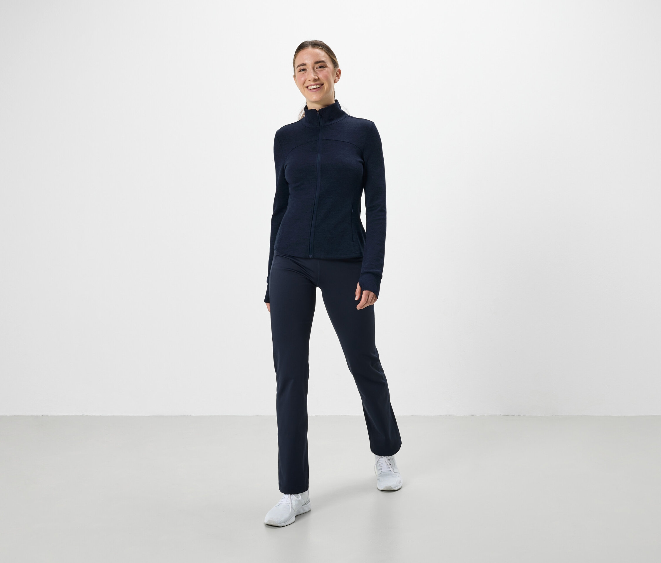 Kobieta ma na sobie granatowy strój sportowy i białe tenisówki.