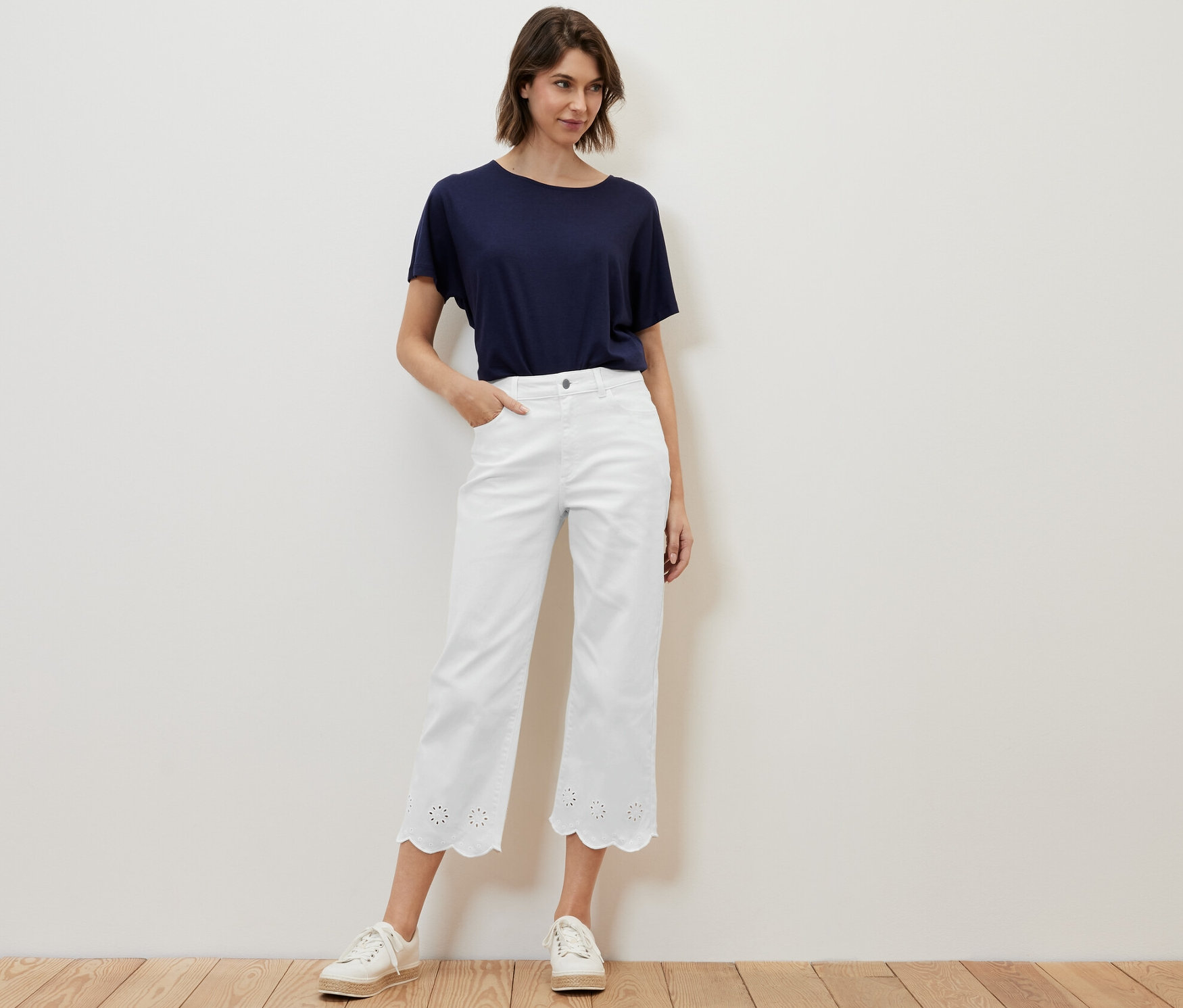 Kobieta pozuje w białych dżinsach z haftem ażurowym i niebieskiej koszulce.