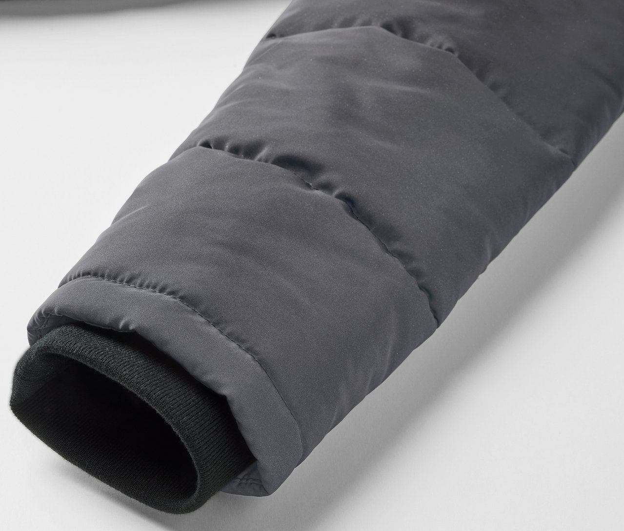 Zbliżenie na rękaw szarej kurtki pikowanej z elementami odblaskowymi i czarnym mankietem.