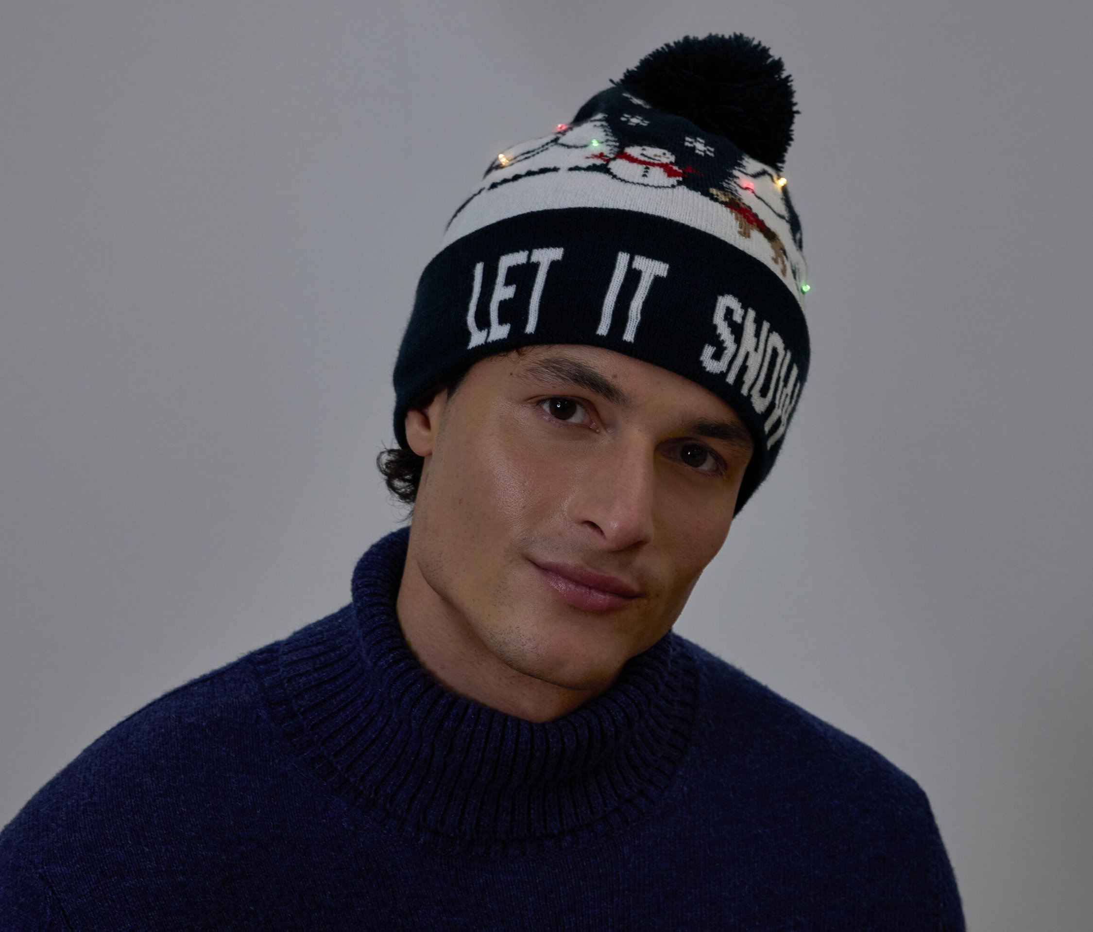 Portret mężczyzny w czapce świątecznej z napisem LET IT SNOW i małymi światełkami.