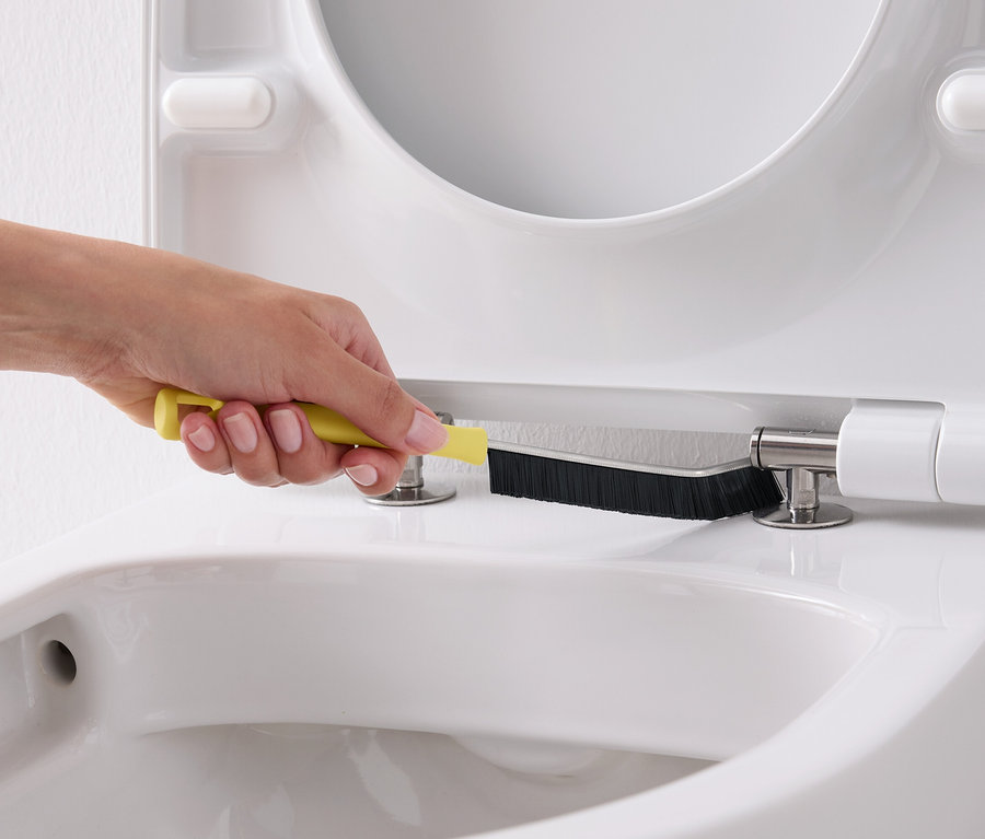 Ręka czyści białą deskę sedesową żółtą szczotką.