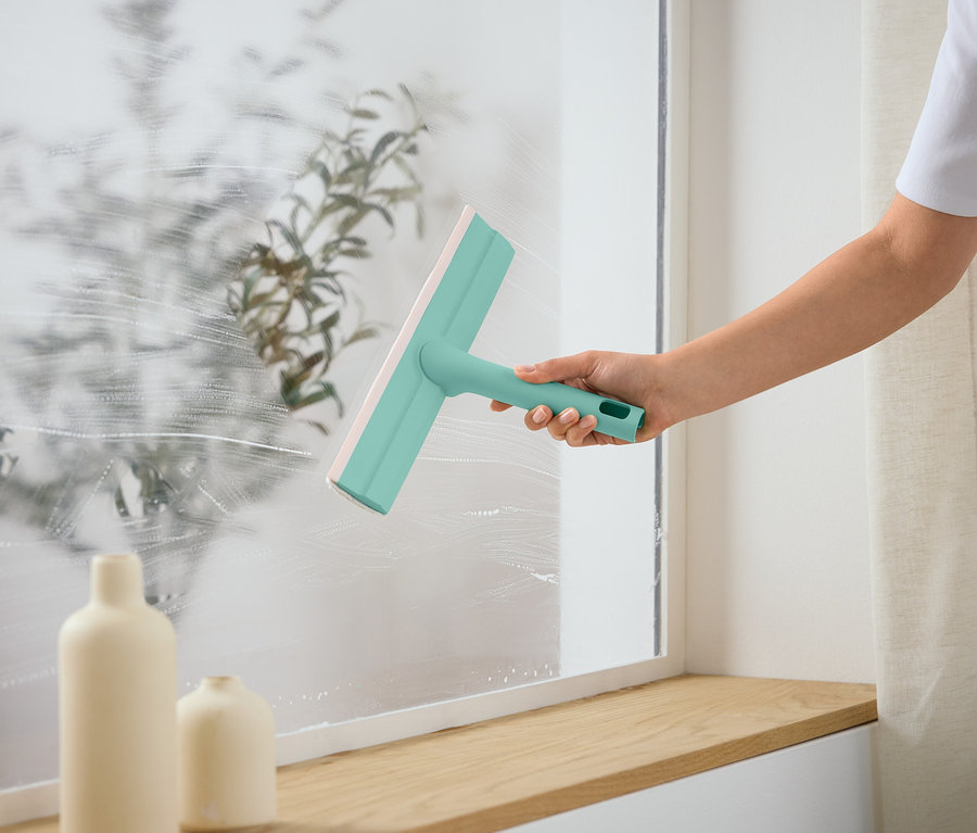 Osoba czyści okno za pomocą ściągaczki do szyb.