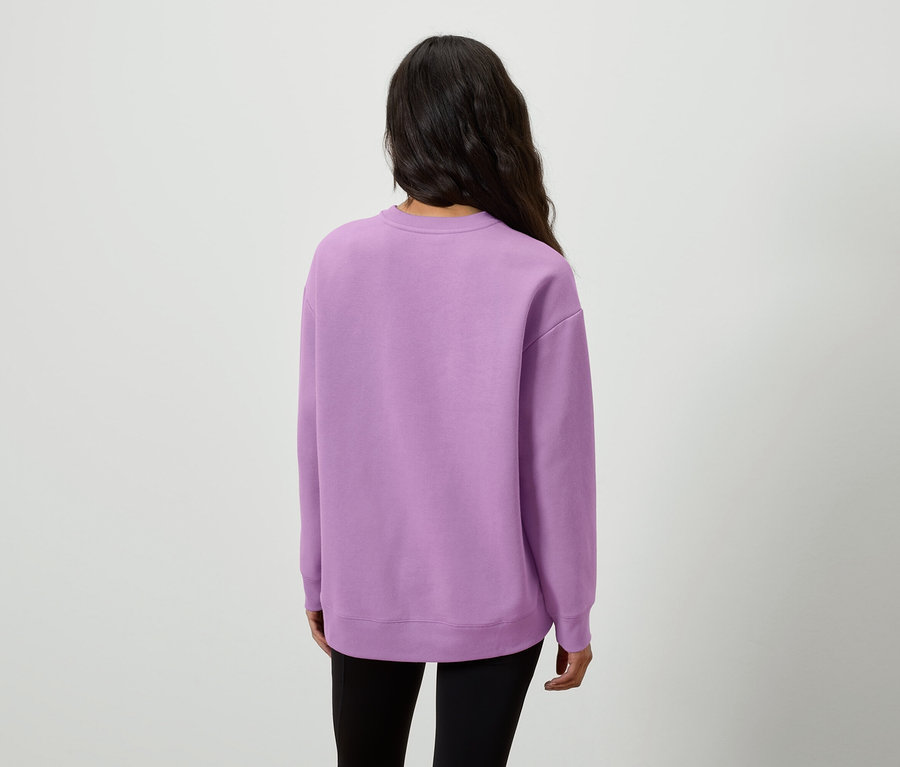 Widok z tyłu kobiety z długimi, ciemnymi włosami w liliowej bluzie i czarnych legginsach.