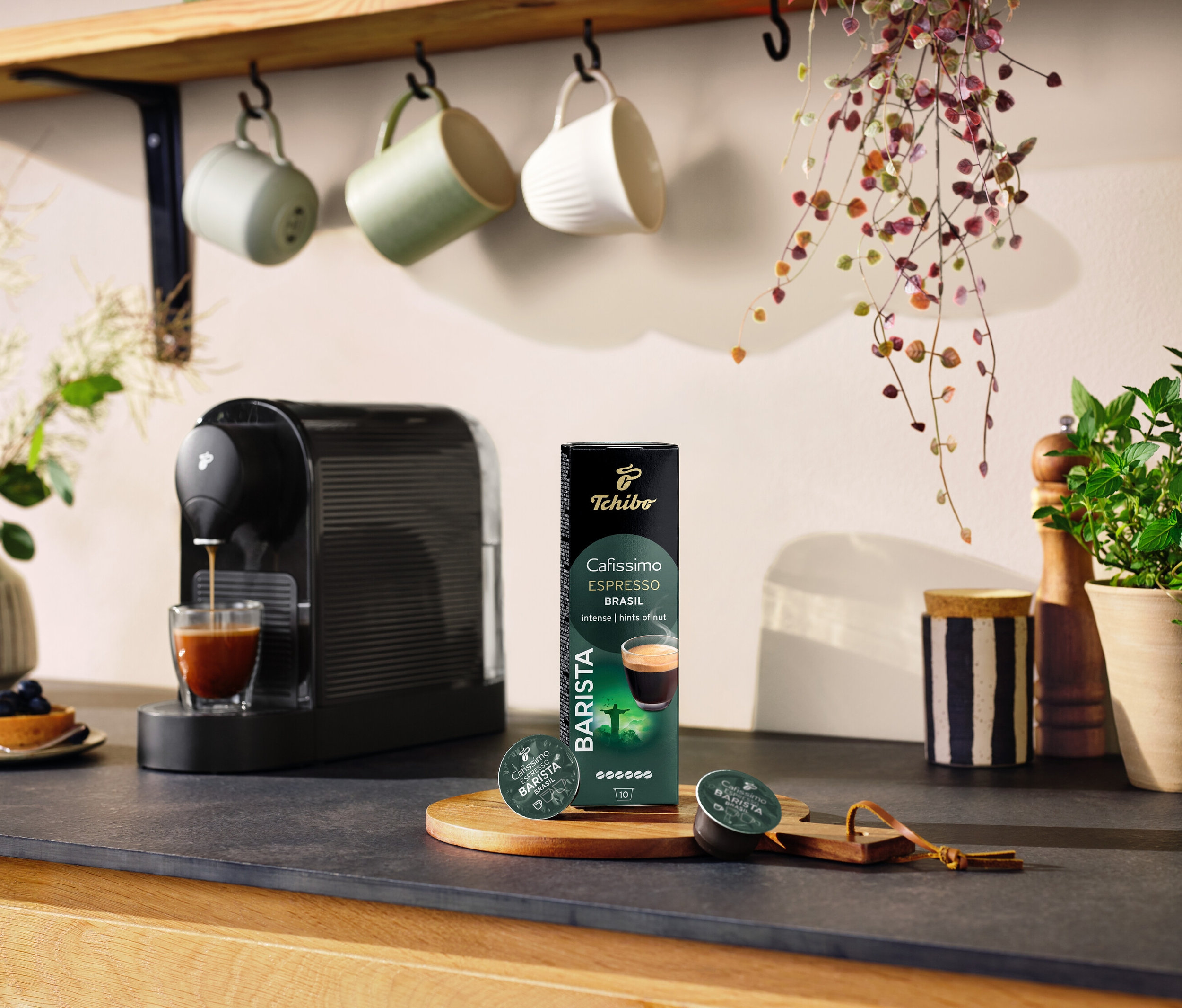 Czarny ekspres do kawy przygotowuje kawę do szklanki obok opakowania kapsułek BARISTA Espresso Brasil – 10 kapsułek.