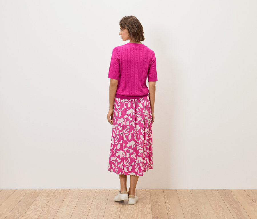 Kobieta stoi tyłem, ma na sobie różowy top i spódnicę w kwiaty.