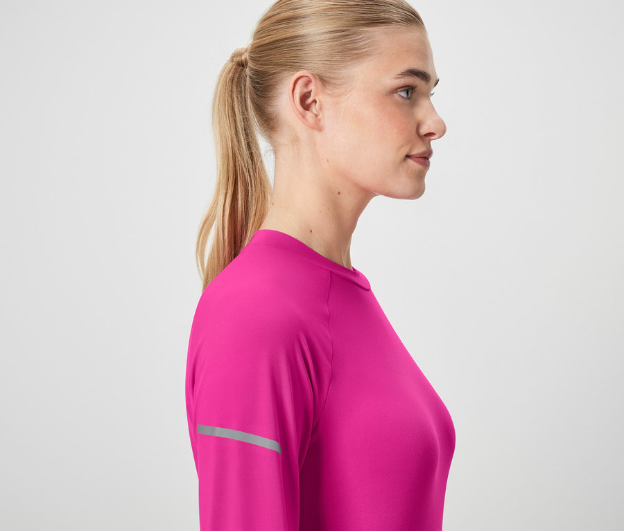 Profil kobiety z blond włosami związanymi w kucyk, ubranej w różową koszulkę z długim rękawem.