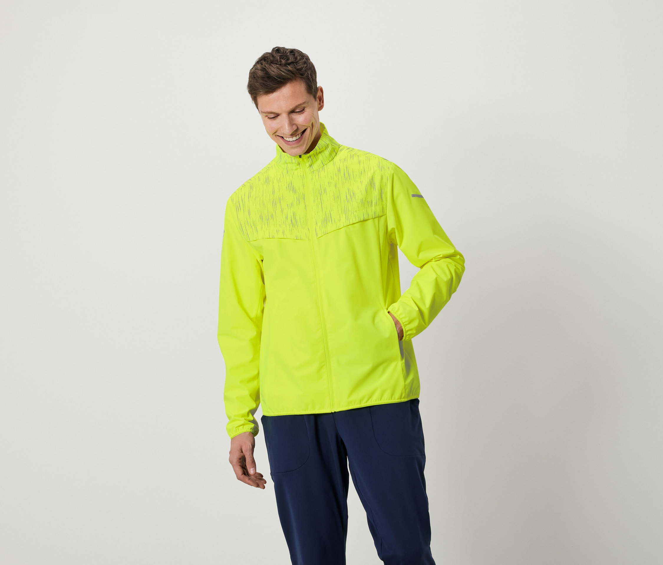 Uśmiechnięty mężczyzna pozuje w neonowożółtej kurtce i granatowych spodniach.