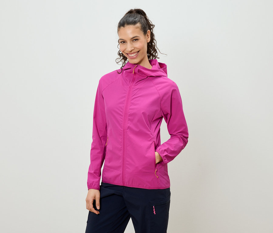 Uśmiechnięta kobieta z włosami upiętymi w kucyk ma na sobie różową kurtkę z kapturem i granatowe spodnie.