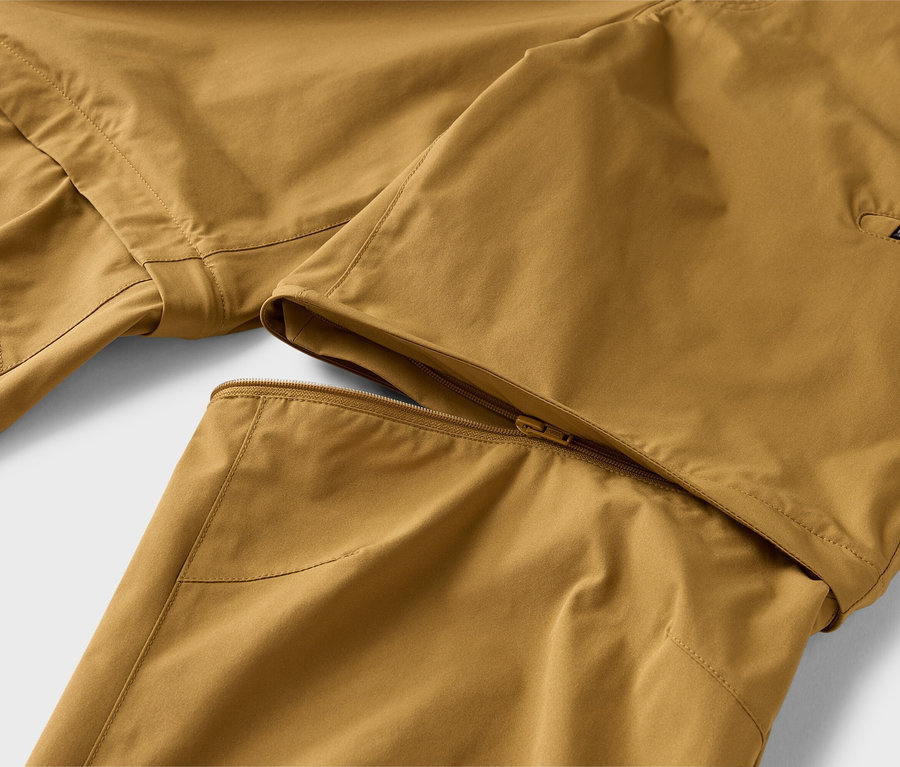 Zbliżenie na parę spodni khaki z odpinaną nogawką, częściowo przymocowaną zamkiem błyskawicznym.