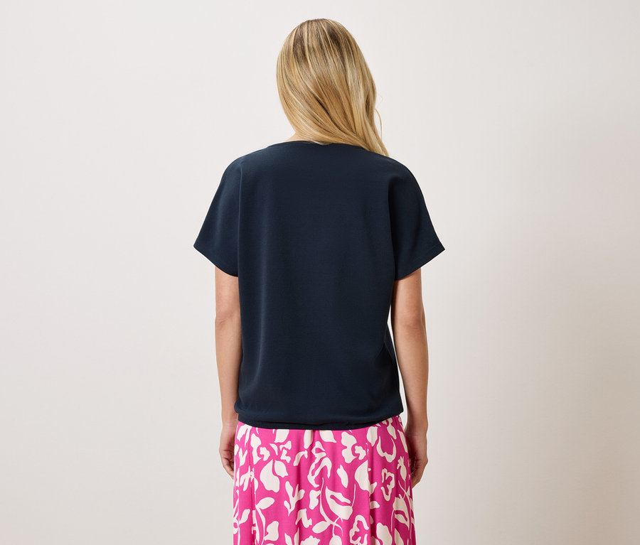 Widok z tyłu blondwłosej kobiety ubranej w granatowy T-shirt i różową spódnicę w kwiaty.