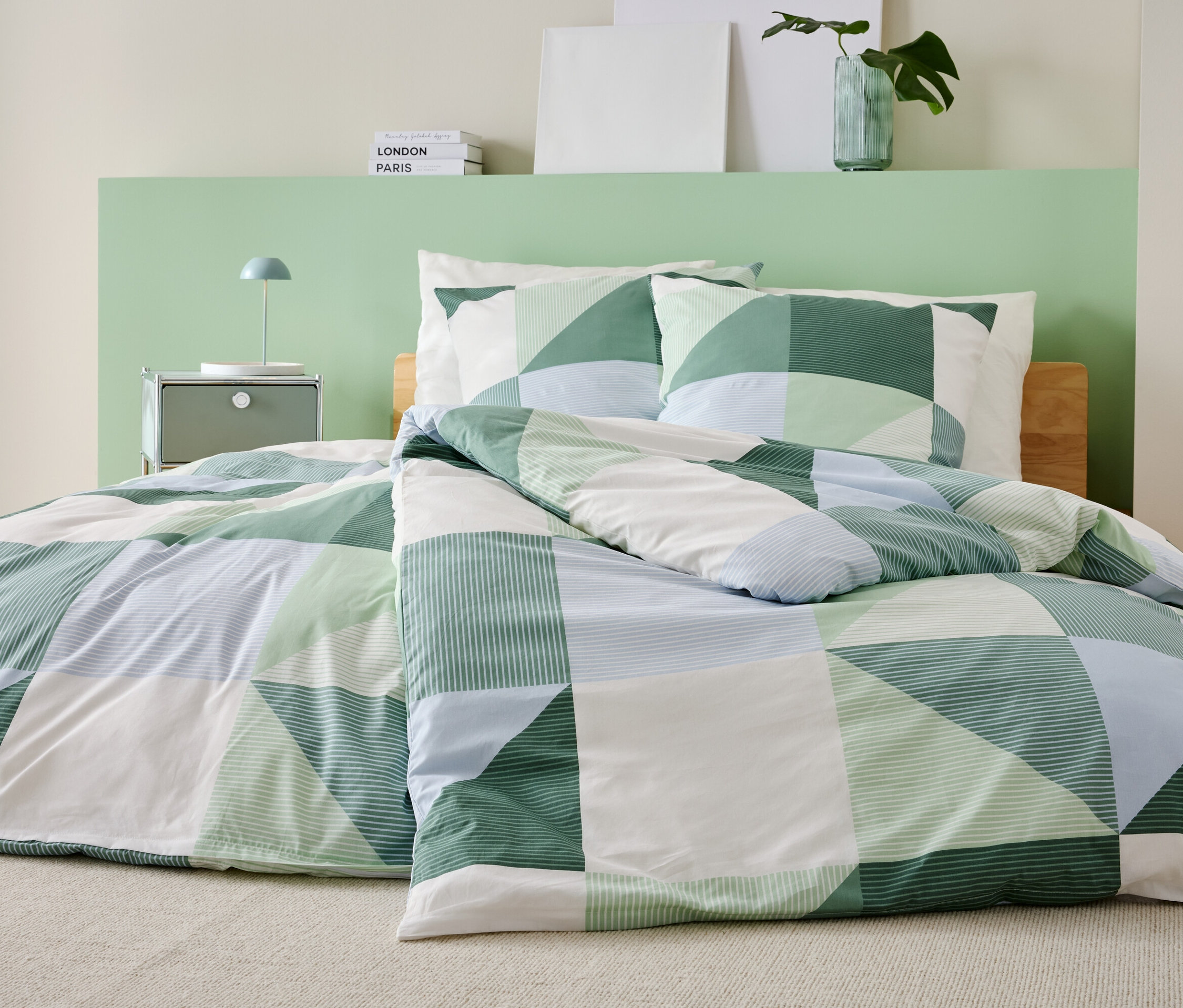 Łóżko z zielono-biało-niebieską patchworkową kołdrą i dopasowanymi poszewkami na poduszki stoi w sypialni.