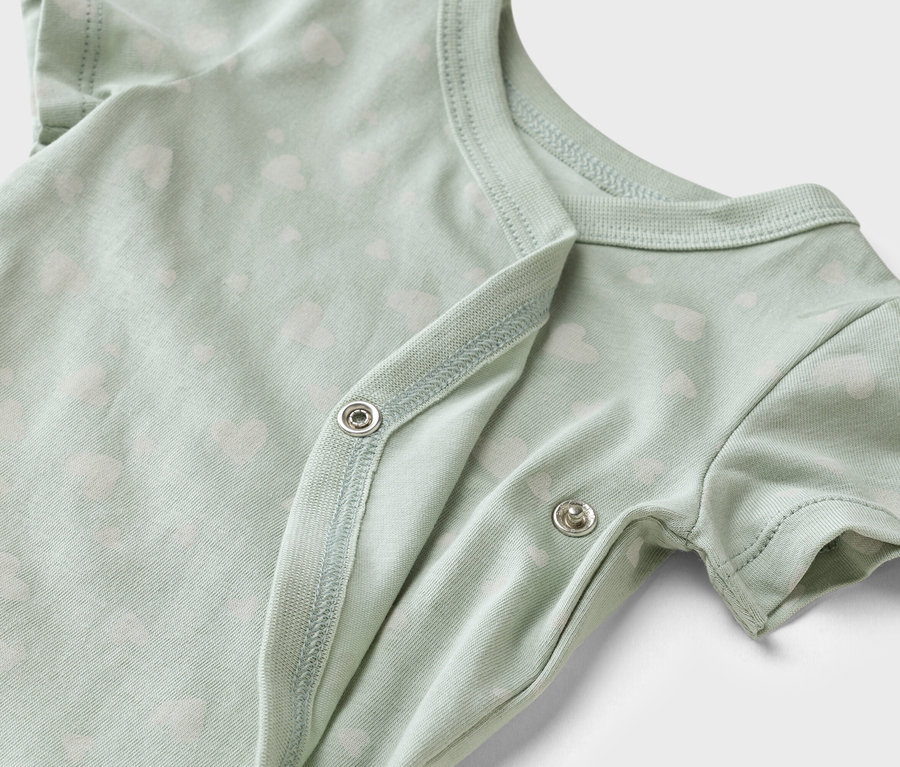 Zbliżenie jasnozielonego body dziecięcego z białym wzorem w serduszka i zatrzaskami.