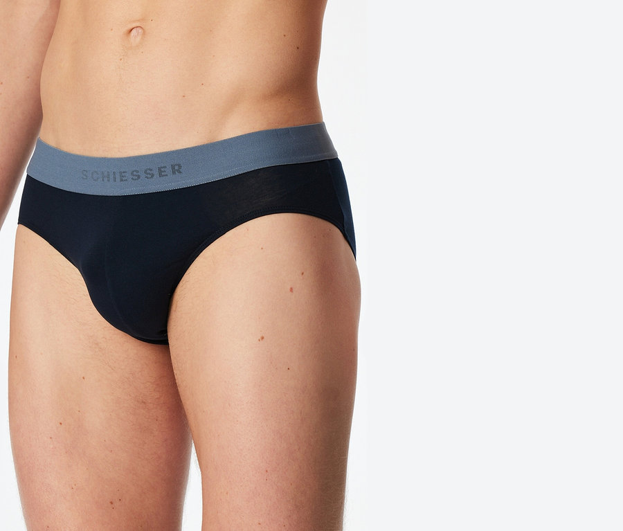 Zbliżenie osoby noszącej czarne slipy Schiesser z szarym pasem.