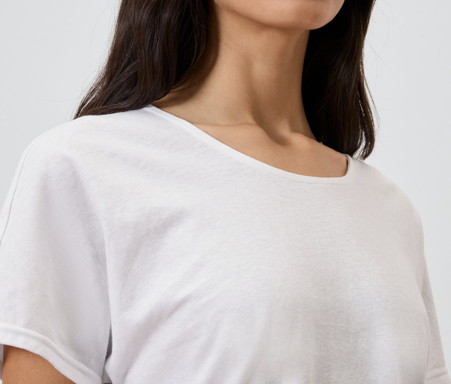 Zbliżenie kobiety o ciemnych włosach w białym T-shircie.