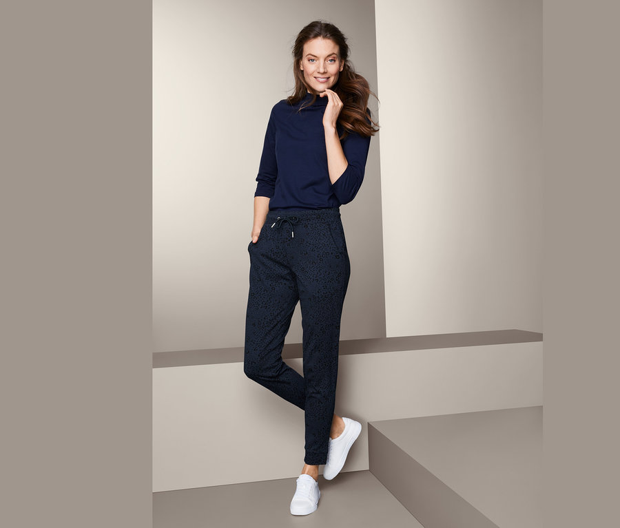 Kobieta pozuje w spodniach dresowych z nadrukiem i bluzce z rękawami trzy czwarte.