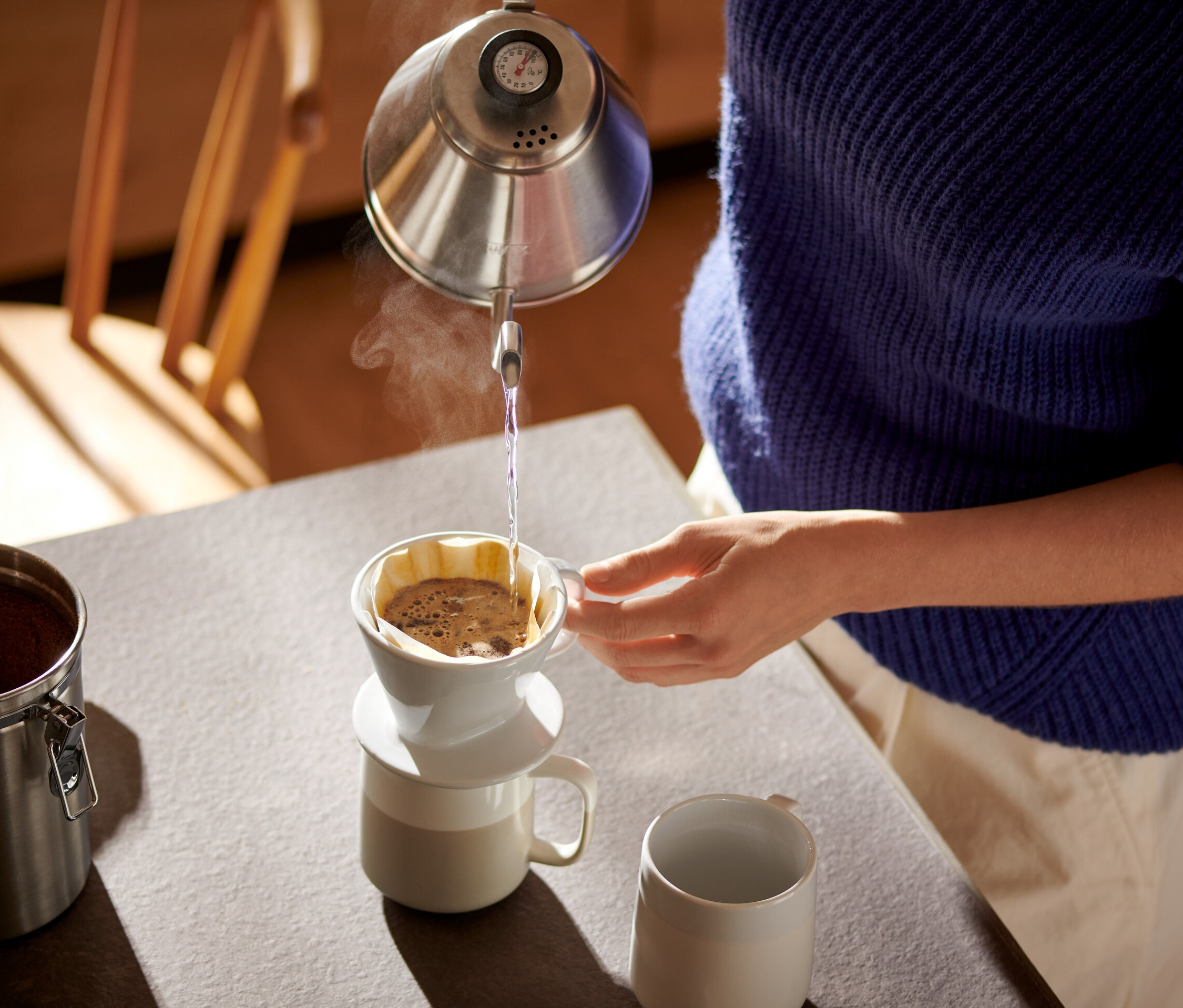 Kobieta nalewa wodę z czajnika do białego ręcznego filtra do kawy w rozm. 101 z papierowymi filtrami do kawy w rozm. 101.