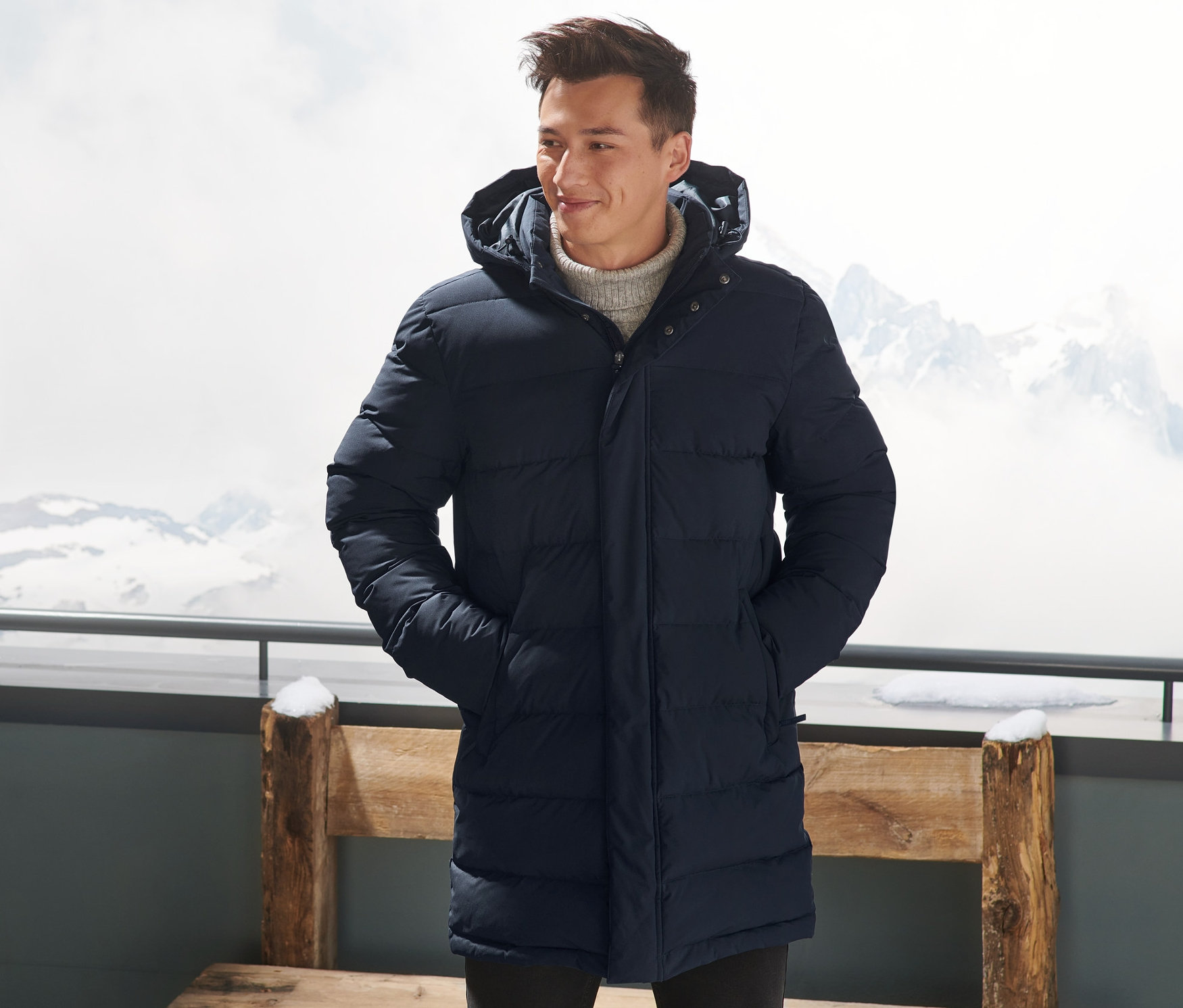 Mężczyzna w granatowej, puchowej parce pikowanej stoi na zewnątrz z rękami w kieszeniach.