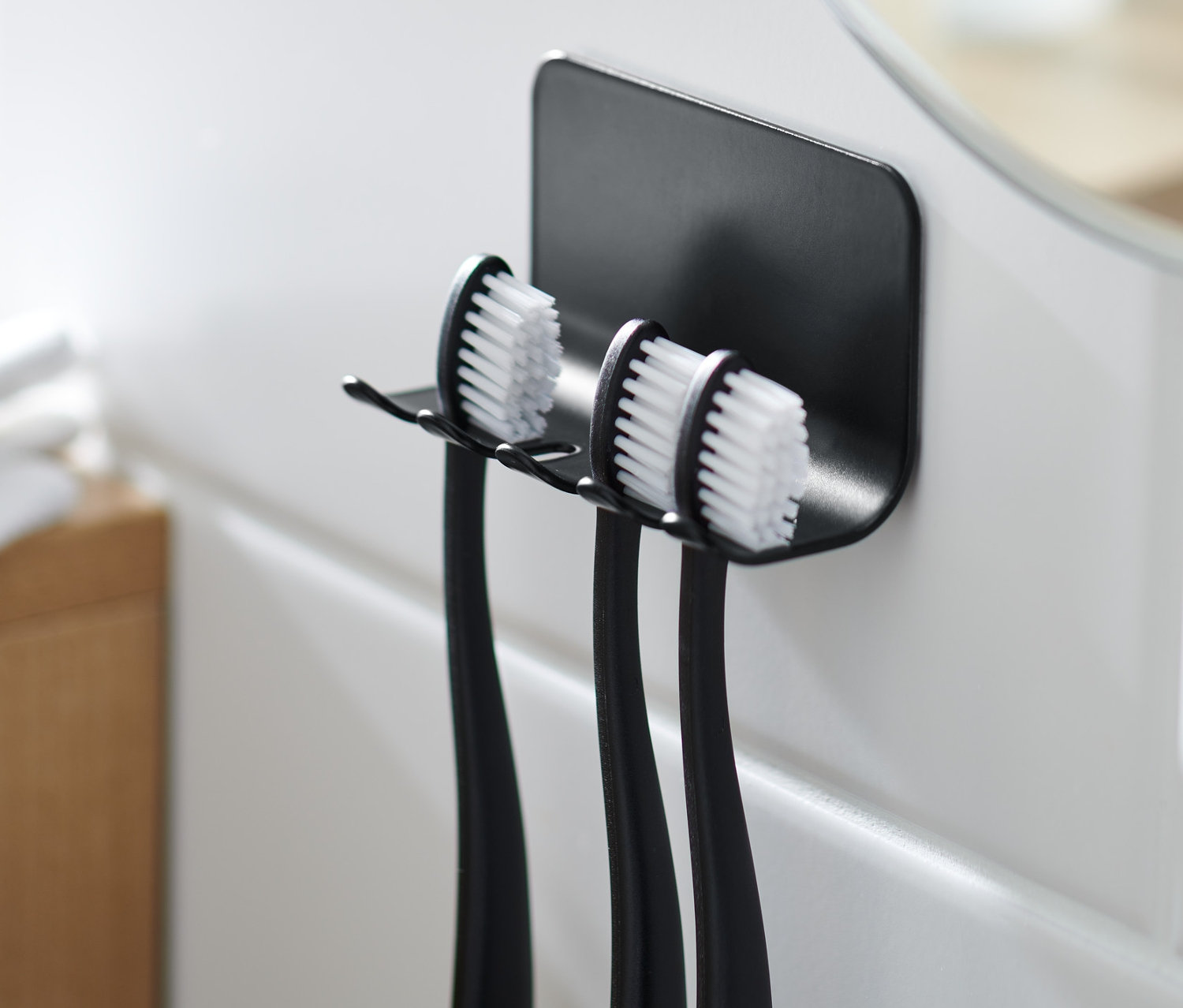 Czarny uchwyt na szczoteczki do zębów z trzema szczoteczkami na białych kafelkach.