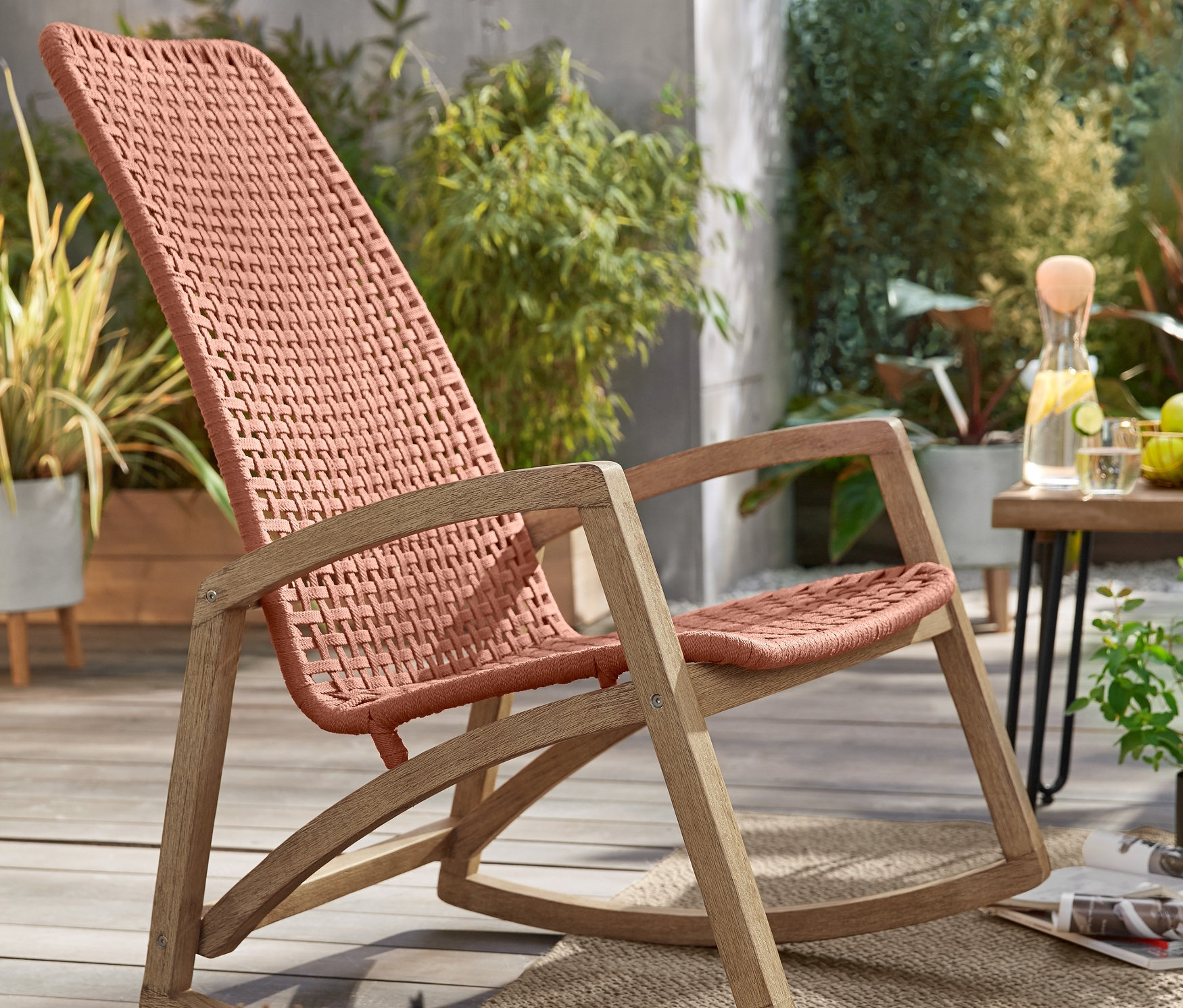 Ogrodowy fotel bujany »rope« i świecznik ze świeczką LED na tarasie. W tle metalowe stoliki stylizowane na betonowe, 2 sztuki i stolik ogrodowy.