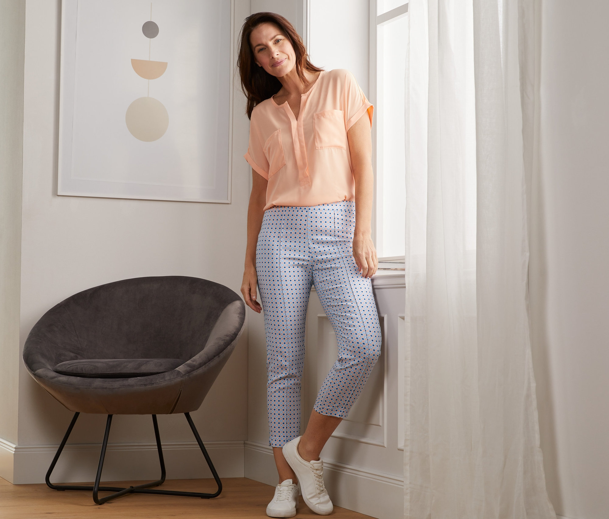 Kobieta opiera się o okno, pozuje w spodniach ze stretchu o długości 7/8, z nadrukiem.