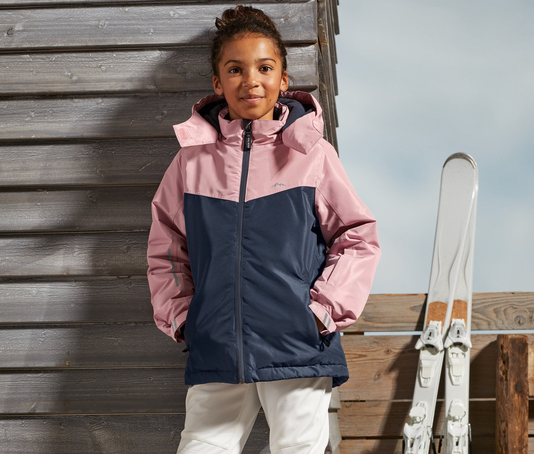 Dziewczyna stoi na zewnątrz w dziewczęcej kurtce narciarskiej i spodniach narciarskich.
