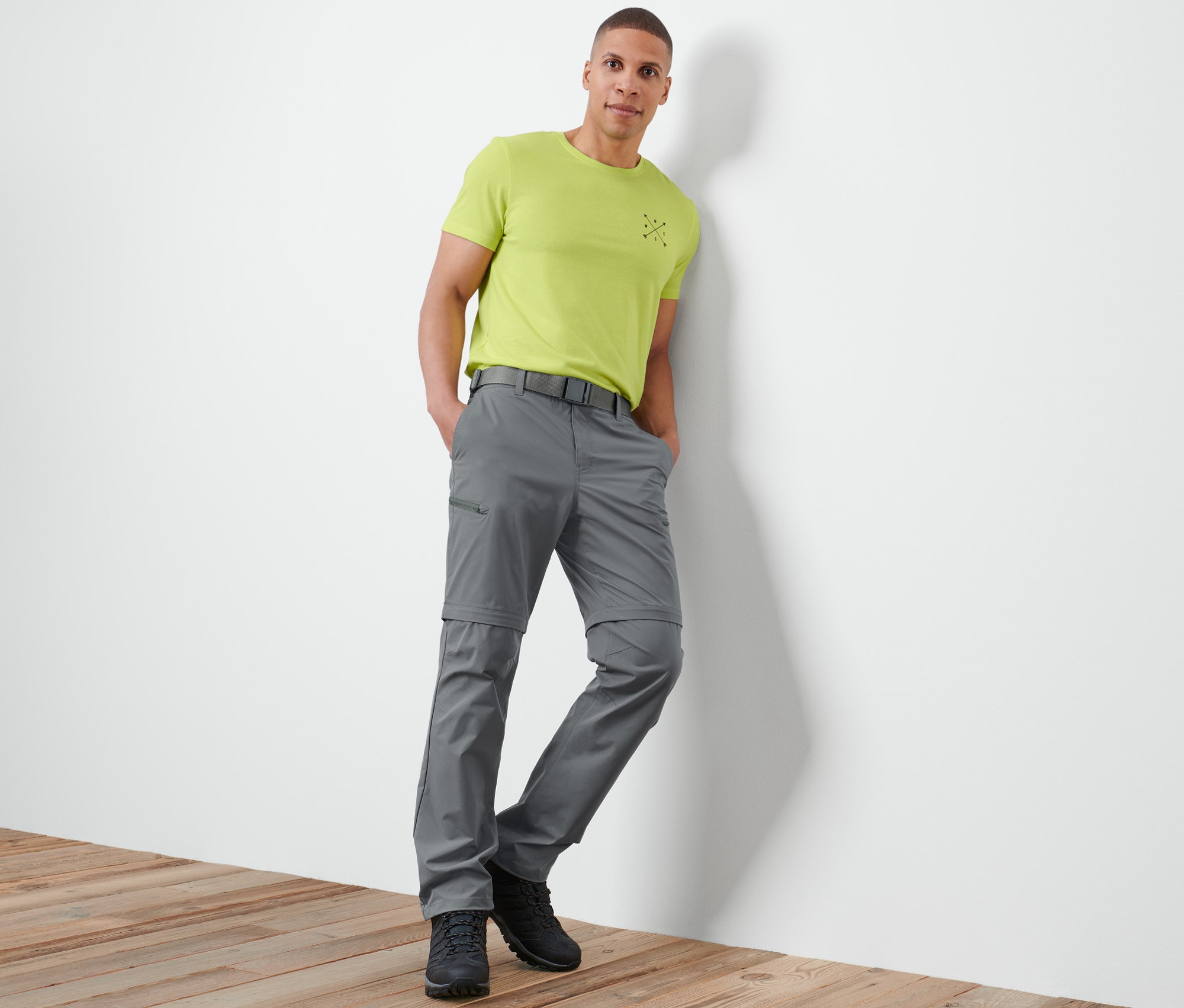 Mężczyzna oparty o ścianę ma na sobie szare spodnie funkcyjne 2 w 1.