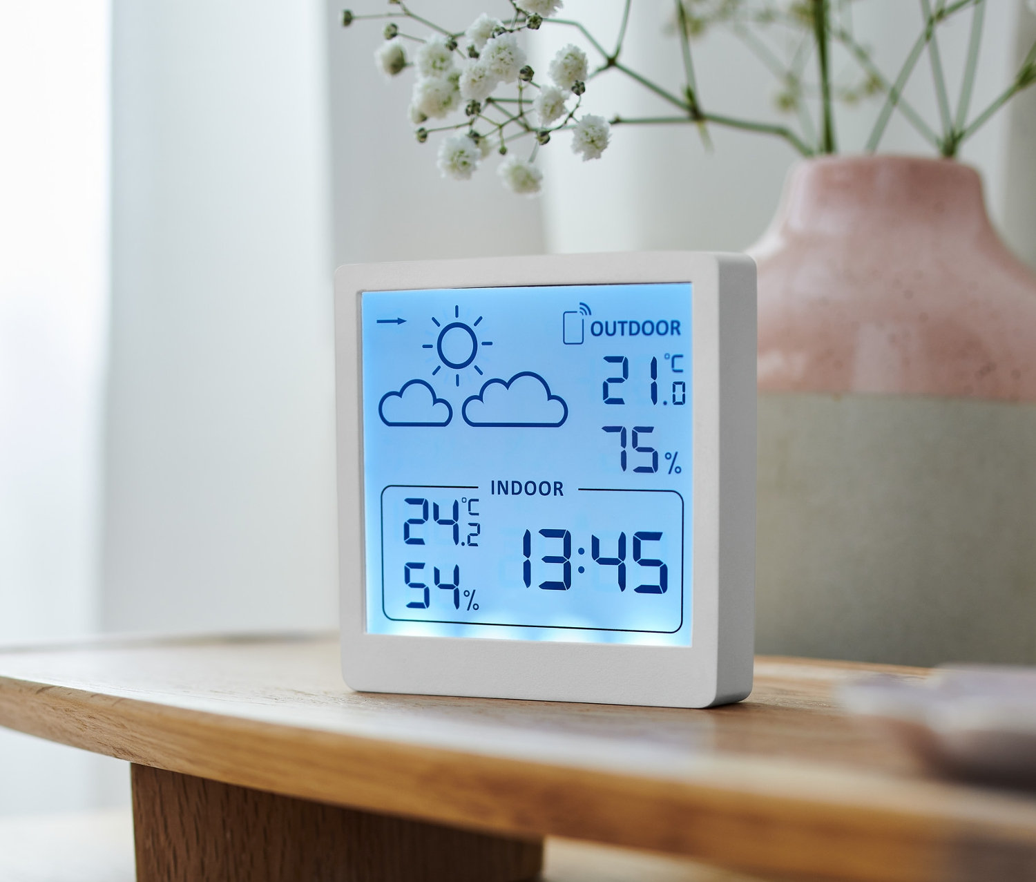 Biała stacja pogodowa wyświetla temperaturę wewnątrz i na zewnątrz oraz wilgotność powietrza.
