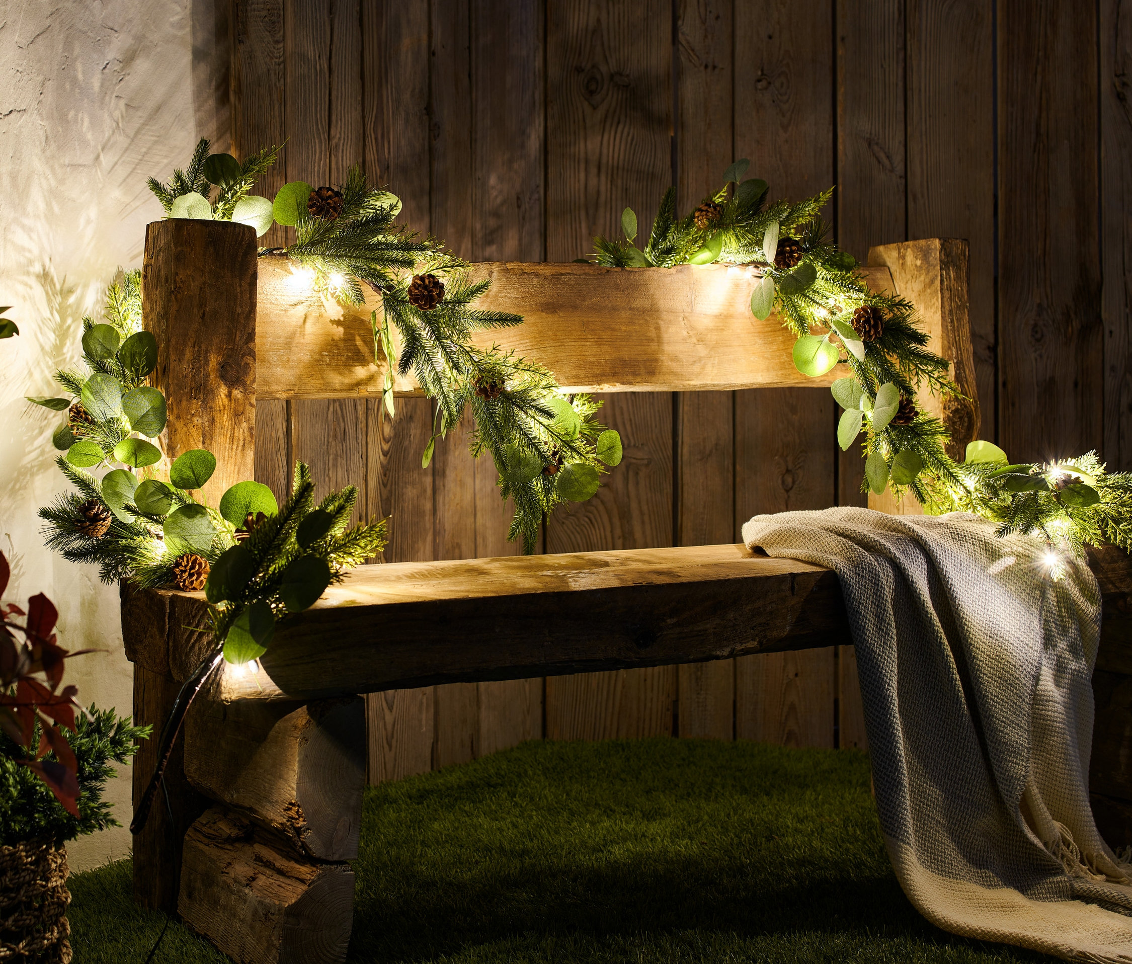 Drewniana ławka ozdobiona girlandą choinkową LED, z szyszkami.