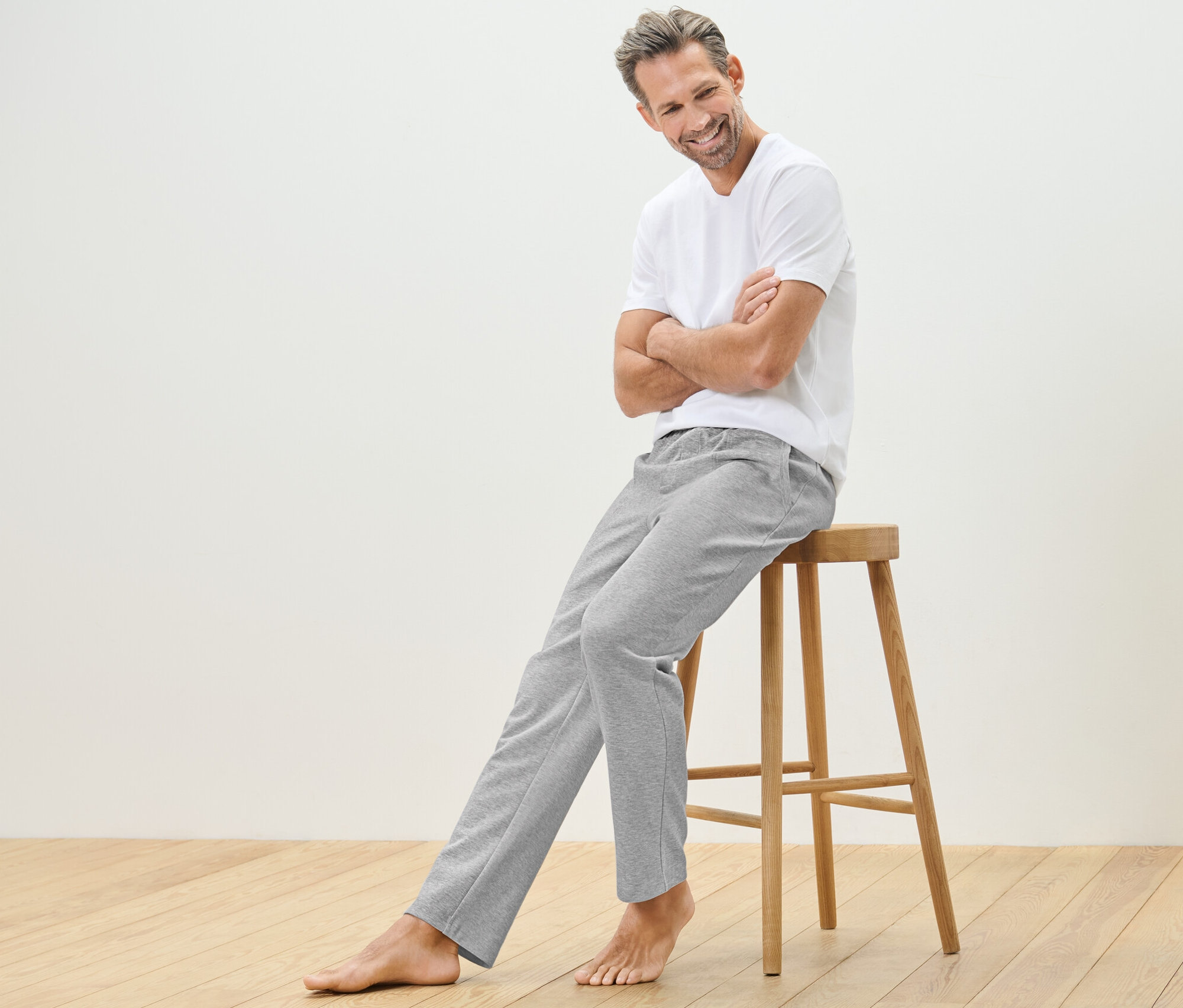 Mężczyzna siedzi na drewnianym stołku i ma na sobie spodnie rekreacyjne i t-shirt.