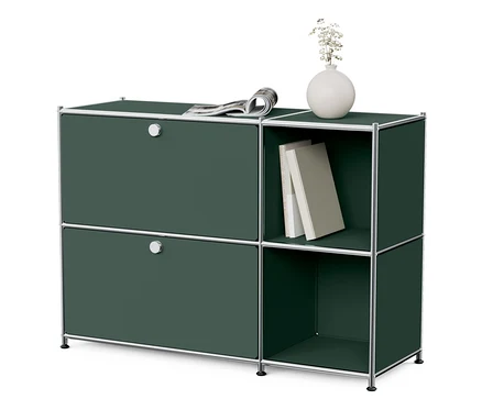 Oliwkowa metalowa szafka typu sideboard „CN3” z 2 klapami. Na szafce leży gazeta, a obok szafki znajduje się otwarta półka z książkami i wazonem.