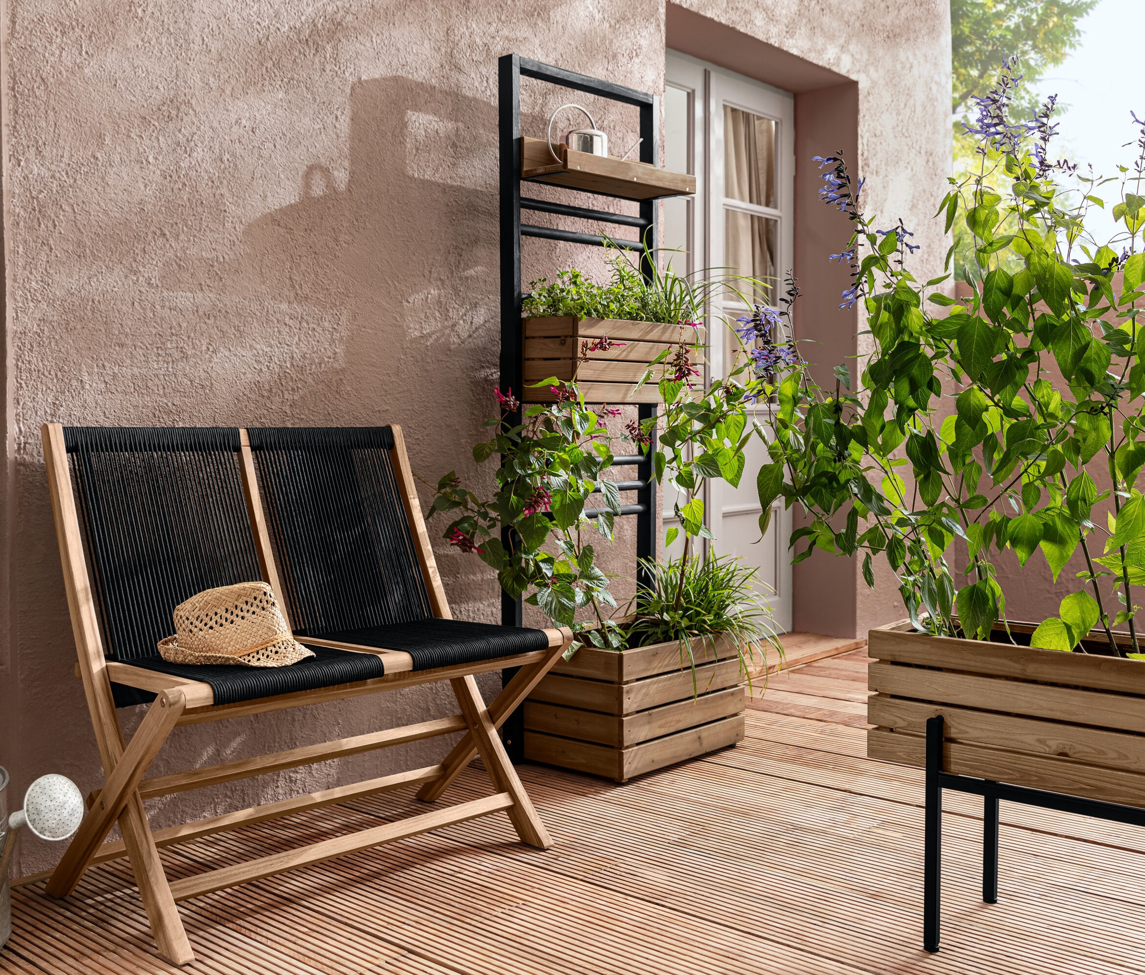 Składana ławka ogrodowa z plecionką tekstylną, regał na rośliny „Elin” i skrzynka na rośliny „Elin” z roślinami na tarasie.