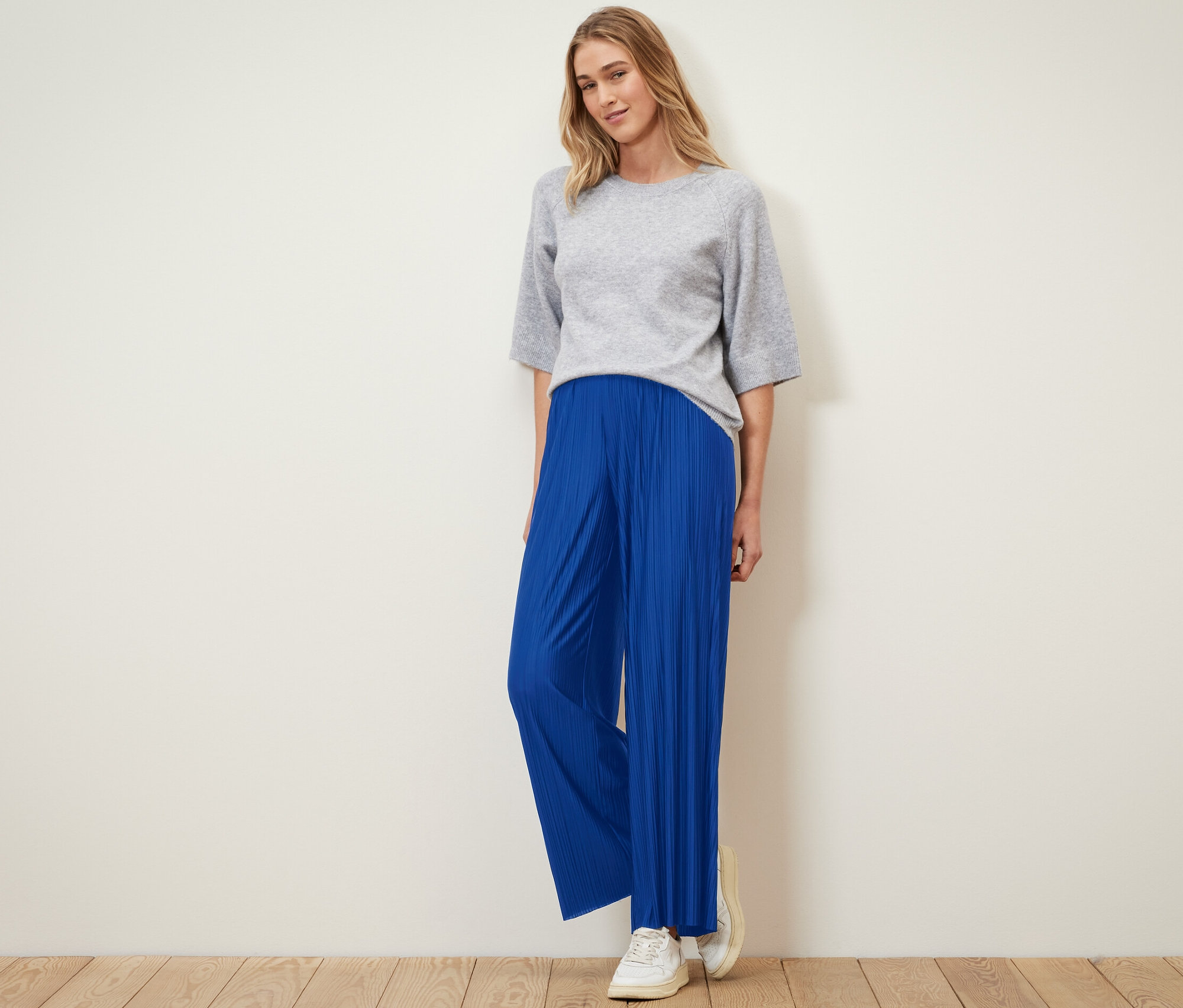 Kobieta stoi w plisowanych spodniach w kolorze kobaltowym i szarym topie.