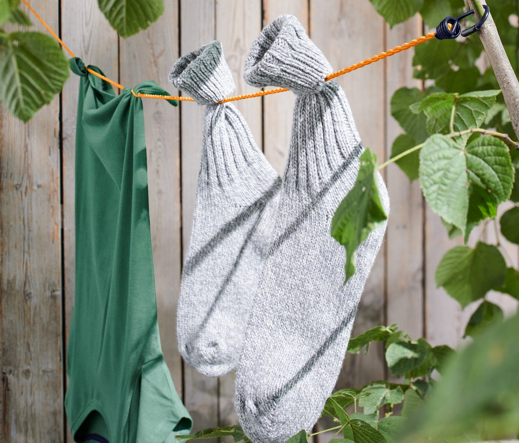 Zielona koszulka i para szarych skarpet wiszą na kempingowej lince na pranie rozpiętej między gałęziami drzew.