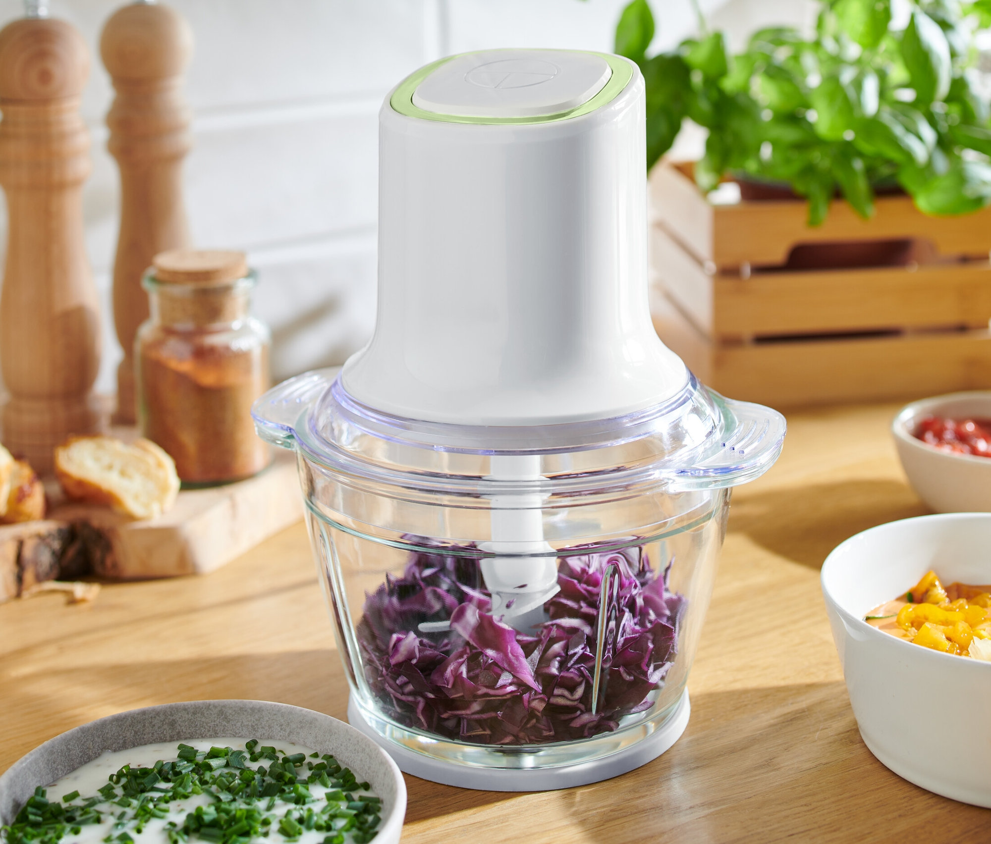 Rozdrabniacz wielofunkcyjny wypełniony poszatkowaną czerwoną kapustą stoi na drewnianym stole między miskami z sosami.