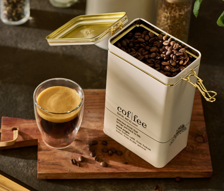 Otwarta puszka na kawę, słownik kawy, wypełniona ziarnami kawy stoi obok szklanki kawy na drewnianej desce.