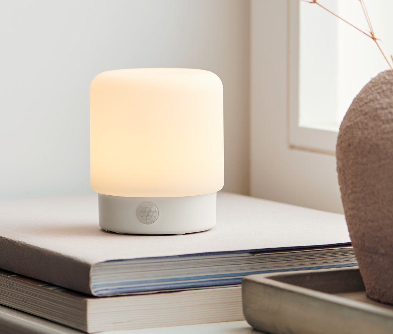 Wielofunkcyjna lampka LED z czujnikiem ruchu stoi na książkach obok wazonu z kwiatami.