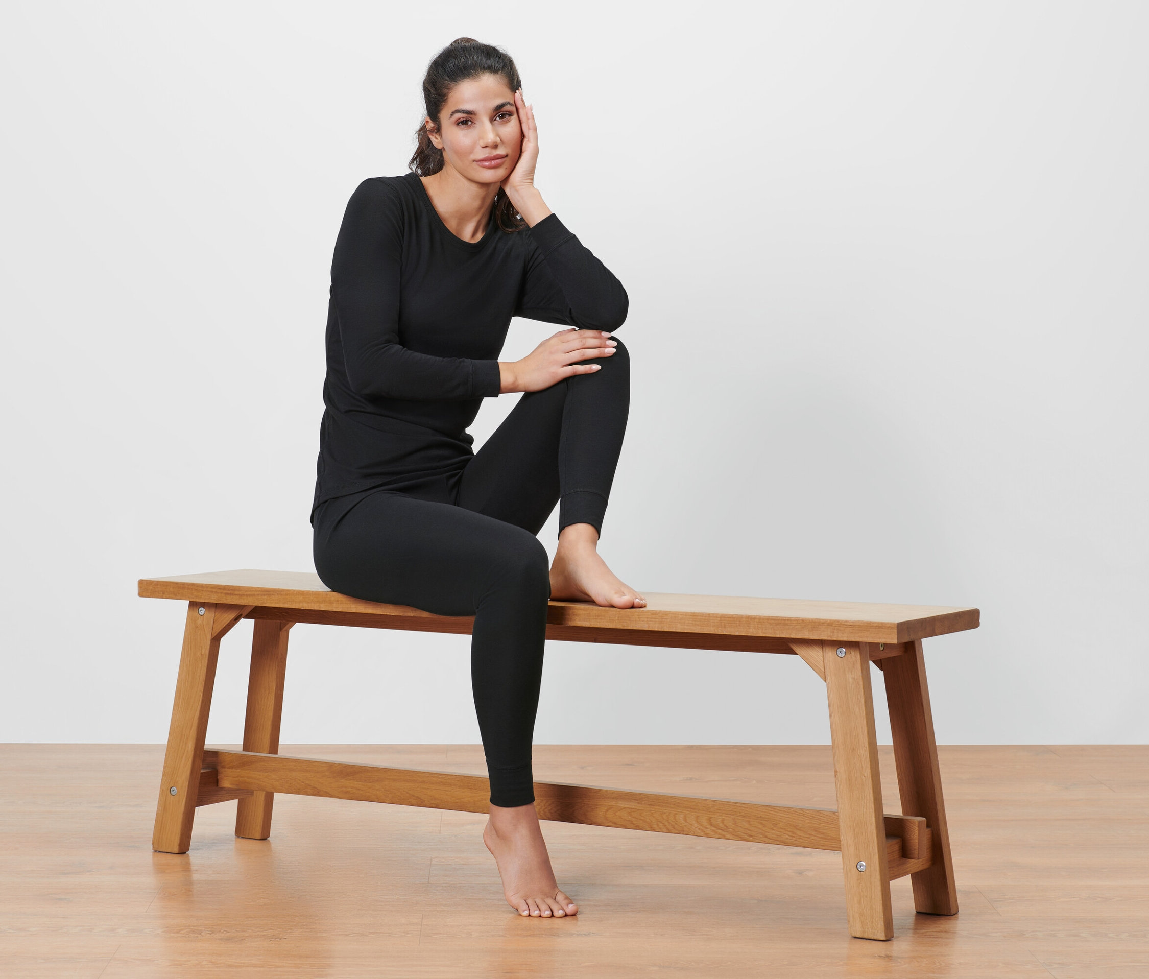 Kobieta siedzi na ławce w czarnej termoaktywnej bieliźnie funkcyjnej.