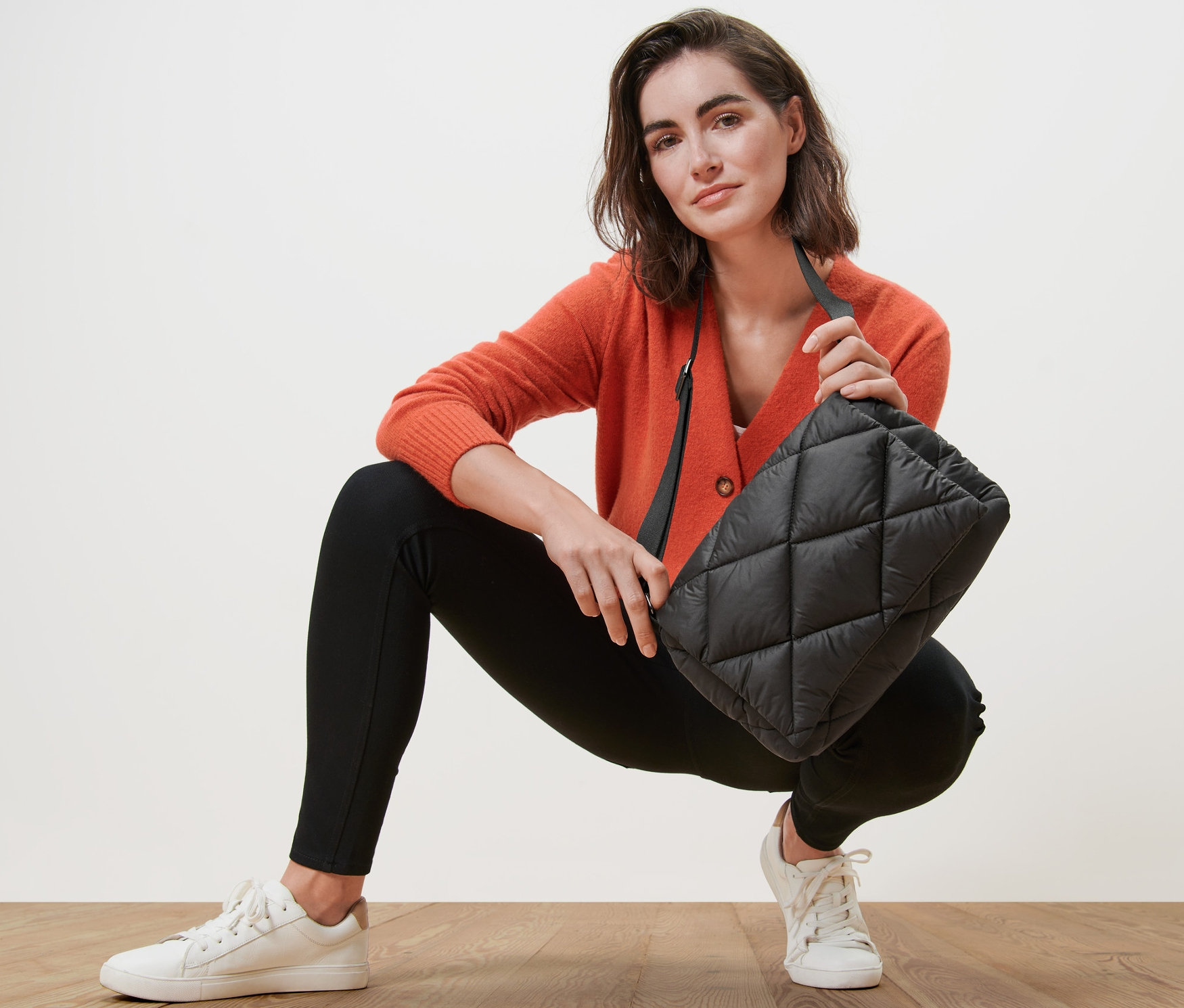 Kobieta w pomarańczowym kardiganie trzyma pikowaną torbę na ramię.