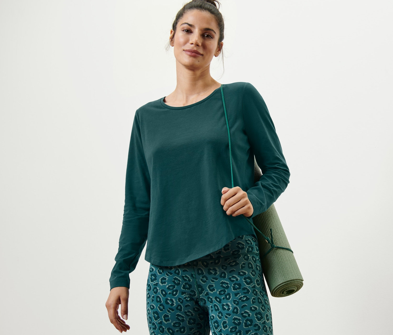 Kobieta ma na sobie zieloną koszulkę sportową z długim rękawem i zieloną matę do jogi.