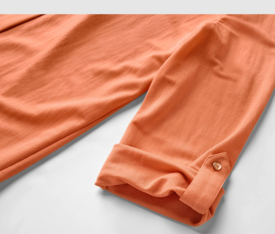 Zbliżenie na brzoskwiniową bluzkę z dżerseju piqué z podwiniętymi rękawami.