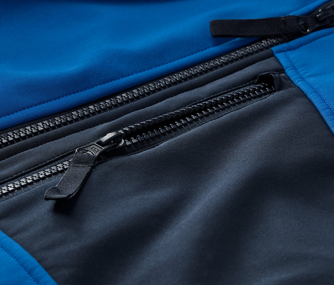 Szczegół niebiesko-czarnej kurtki softshell z zamkami błyskawicznymi.