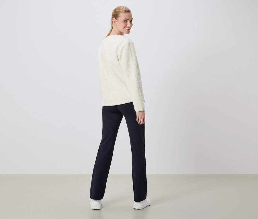 Kobieta patrzy przez ramię, ubrana w kremowy sweter i granatowe spodnie.
