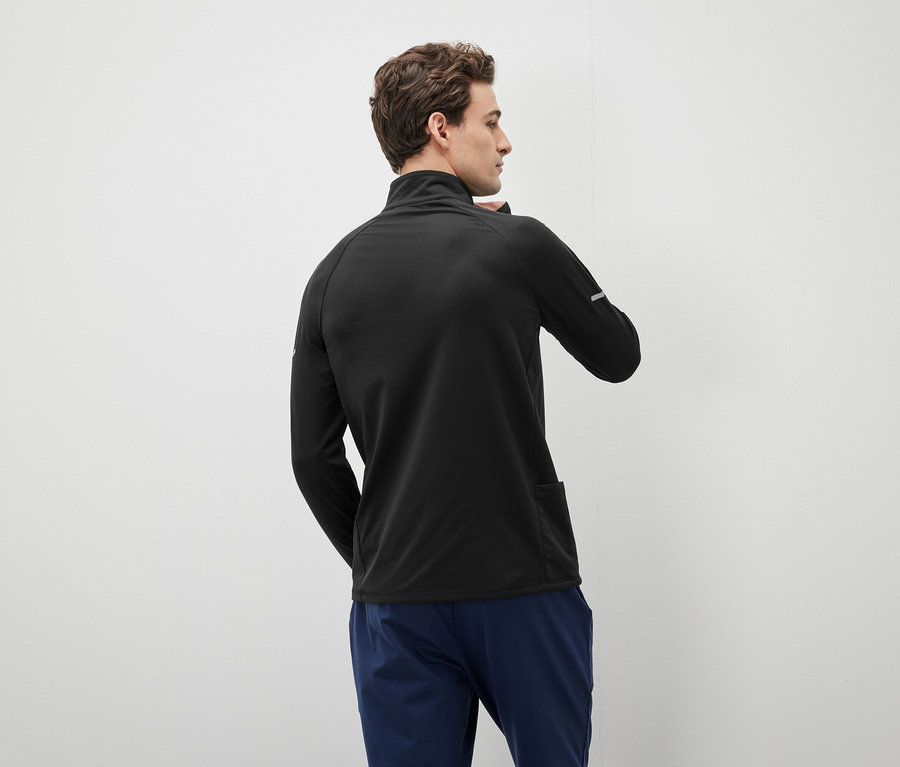 Mężczyzna w czarnym swetrze na zamek i niebieskich spodniach, patrzący w lewo.