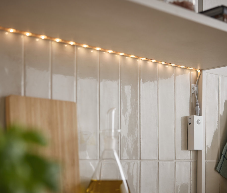 Listwa LED świeci pod szafką na białych płytkach.